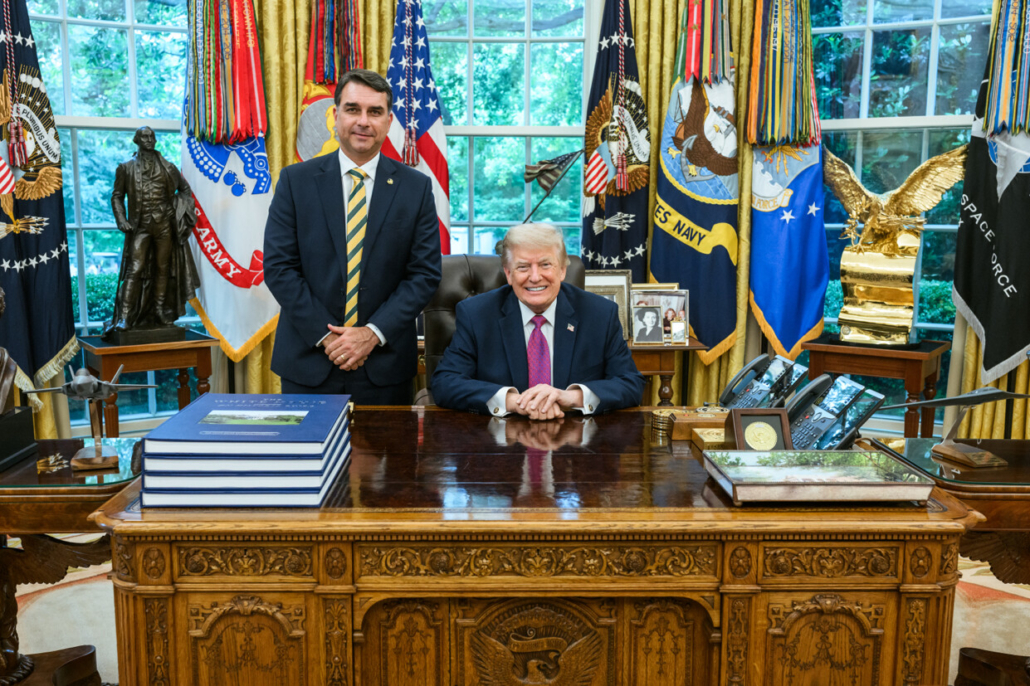 Donald Trump alla scrivania dello Studio Ovale con Flávio Bolsonaro in piedi accanto a lui